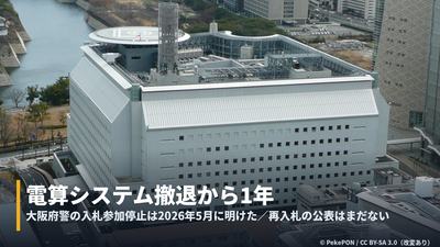 大阪府警察本部の空撮に「電算システム撤退から1年」の字幕帯を重ねたカバー画像